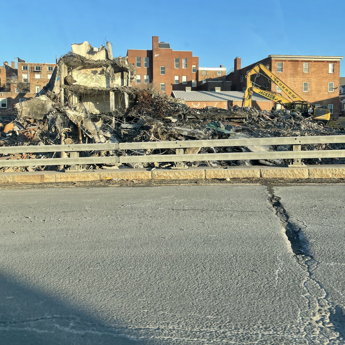 album art for a track called "sibilants hissing in the speakers" - across a lane of a freeway two cranes appear to be demolishing a building