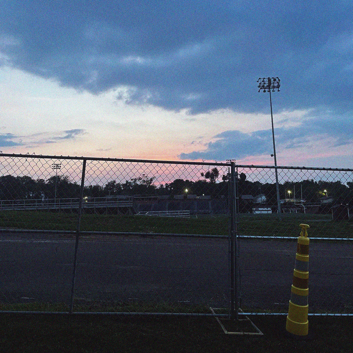 a traffic cone and a chain link fence sit before a beautiful pinky sunset on a football field