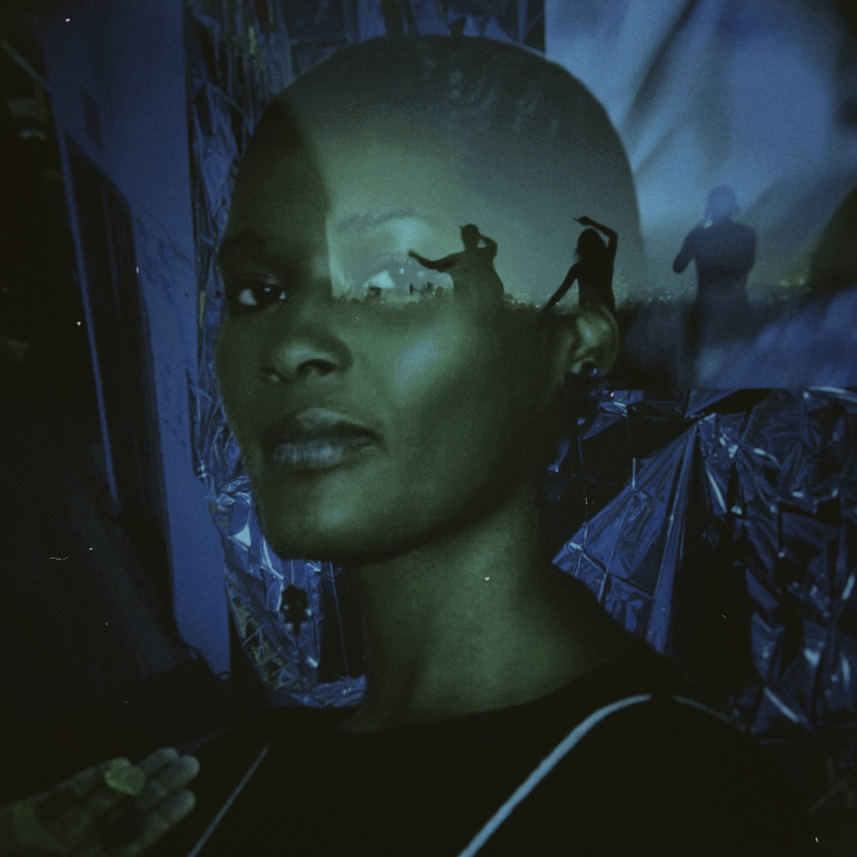 Double-exposed portrait lit green and blue, silhouettes of dancers projected across the subject's brow, crinkled silver foil behind