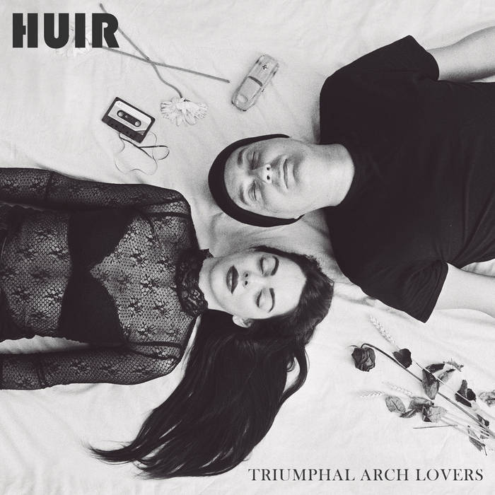 HUIR Triumphal Arch Lovers cover artwork. Two human beings on a bed, heads side-by-side, surrounded by flowers, a tape cassette and a model car. Monochrome shot.